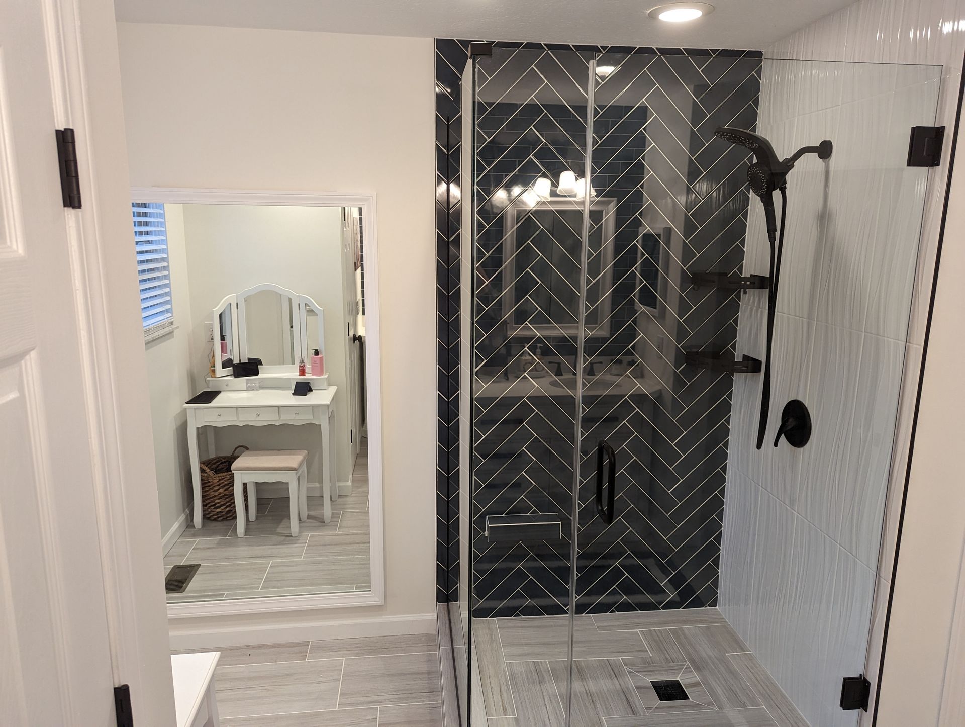 Modern bathroom with black herringbone tile shower, vanity in the mirror, and white walls.