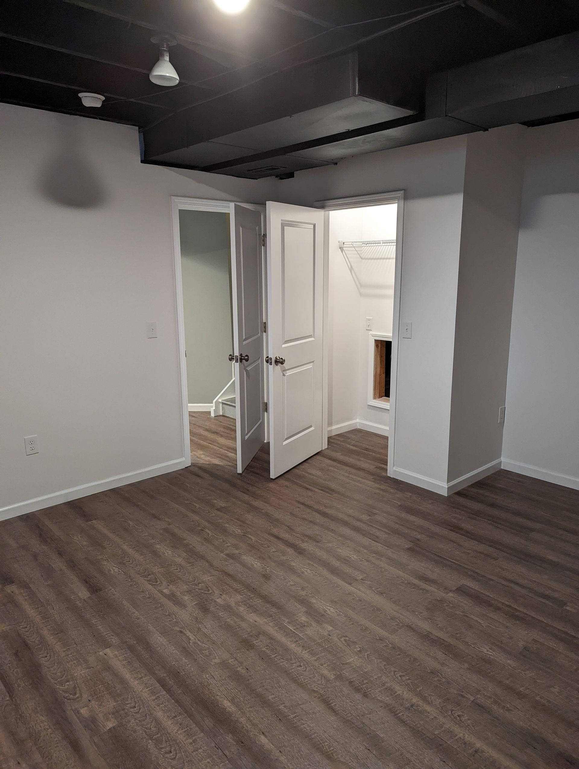 Room with dark wood-look flooring, white walls, and three white doors leading to other rooms.