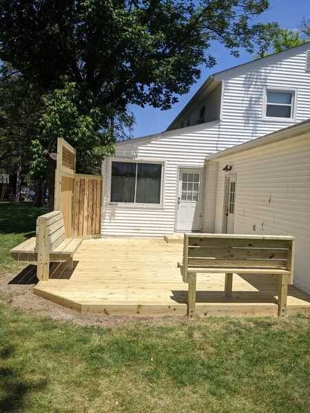 Wooden deck with built-in benches against a white house, with grass in the foreground and a blue sky.