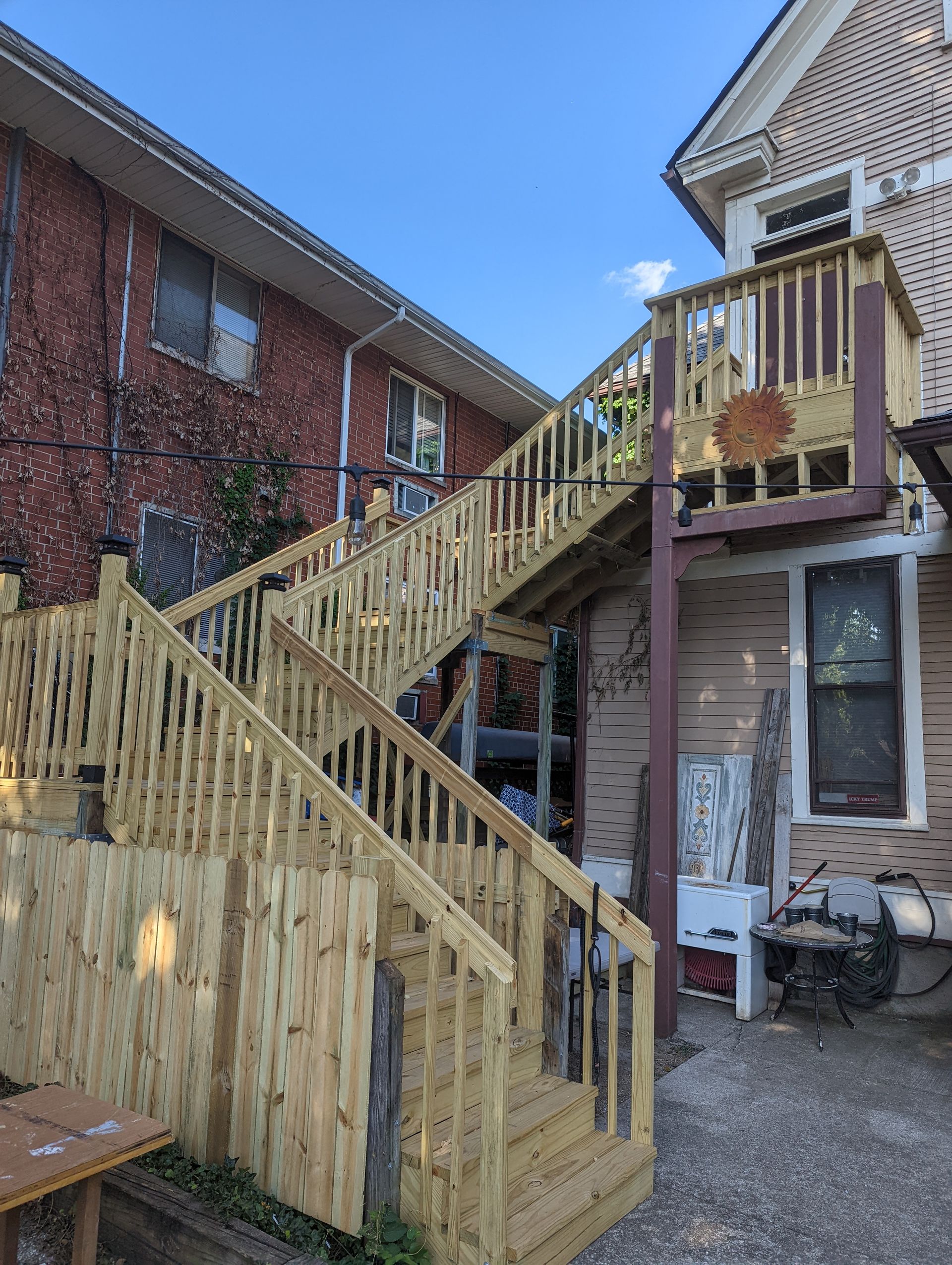 Wooden exterior staircase against brick buildings, leading up to a deck.