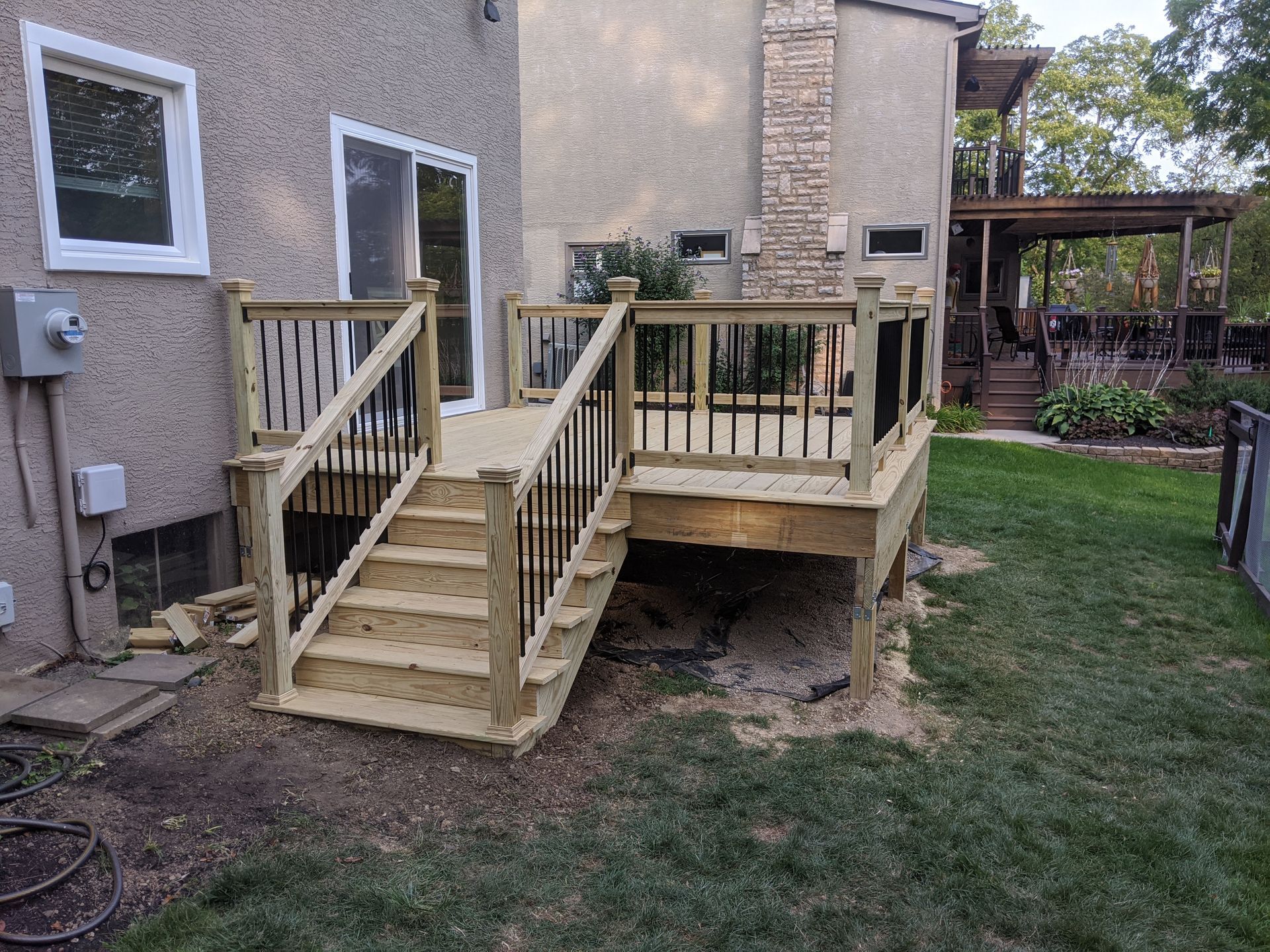 A wooden deck with stairs leading up to it is in the backyard of a house.