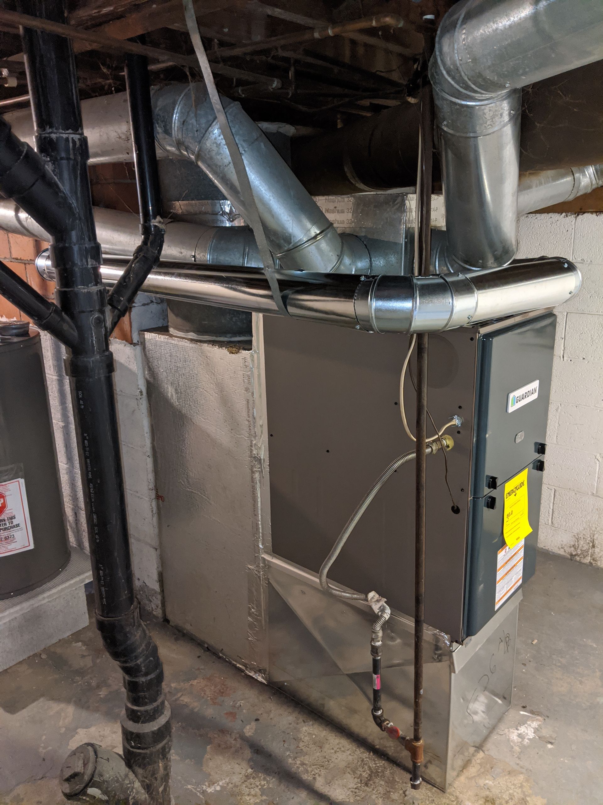 A furnace is sitting in a basement next to pipes.