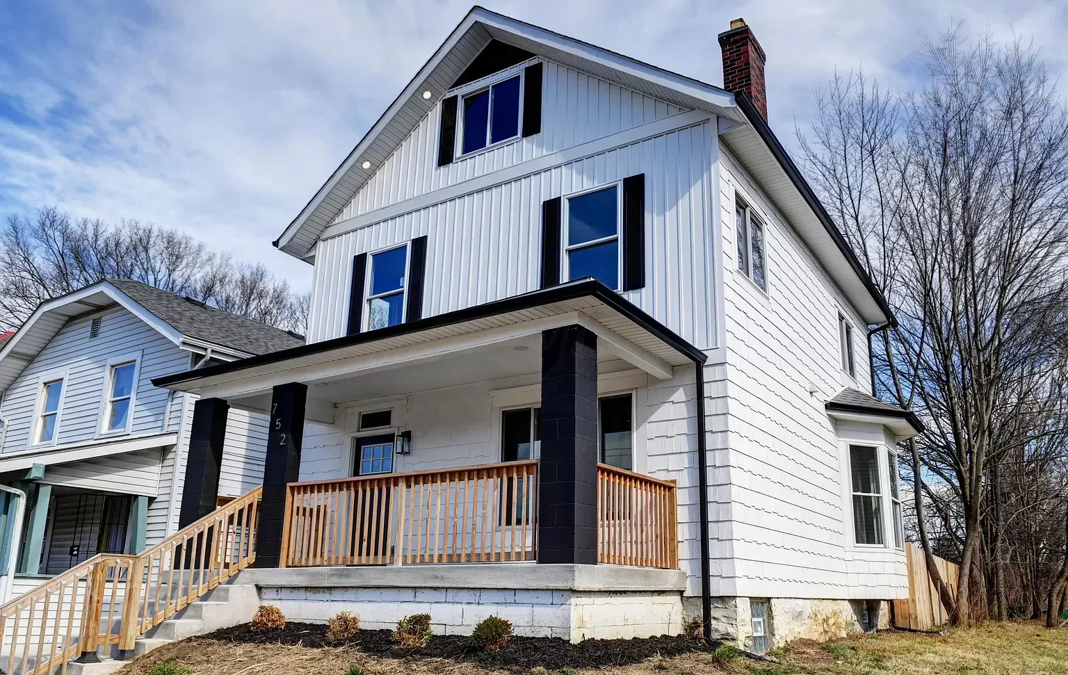 White two-story house with black trim and porch, in a residential neighborhood.