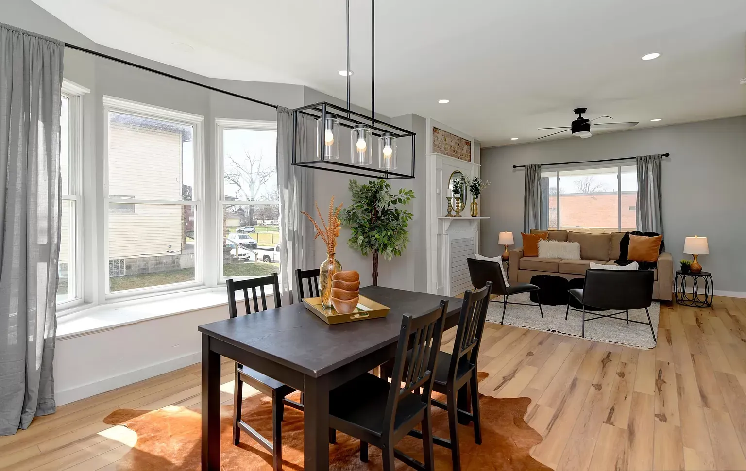 Dining area with dark table and chairs, open to living room with fireplace and bay window.