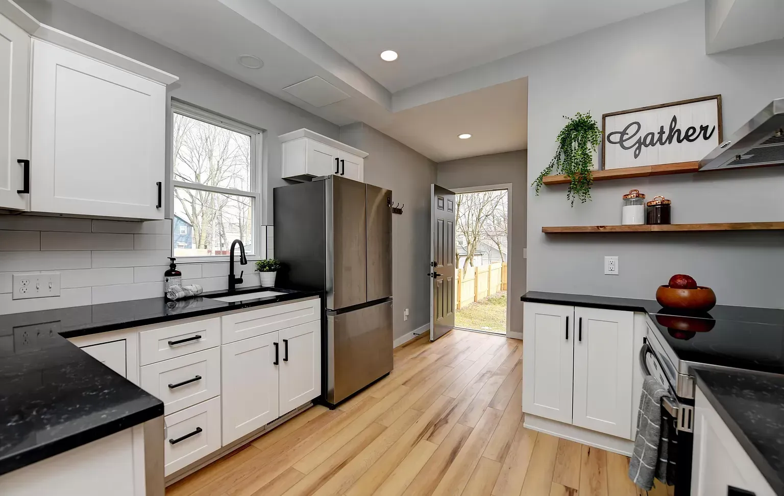 White kitchen with dark countertops, stainless steel appliances, and a door to the backyard.
