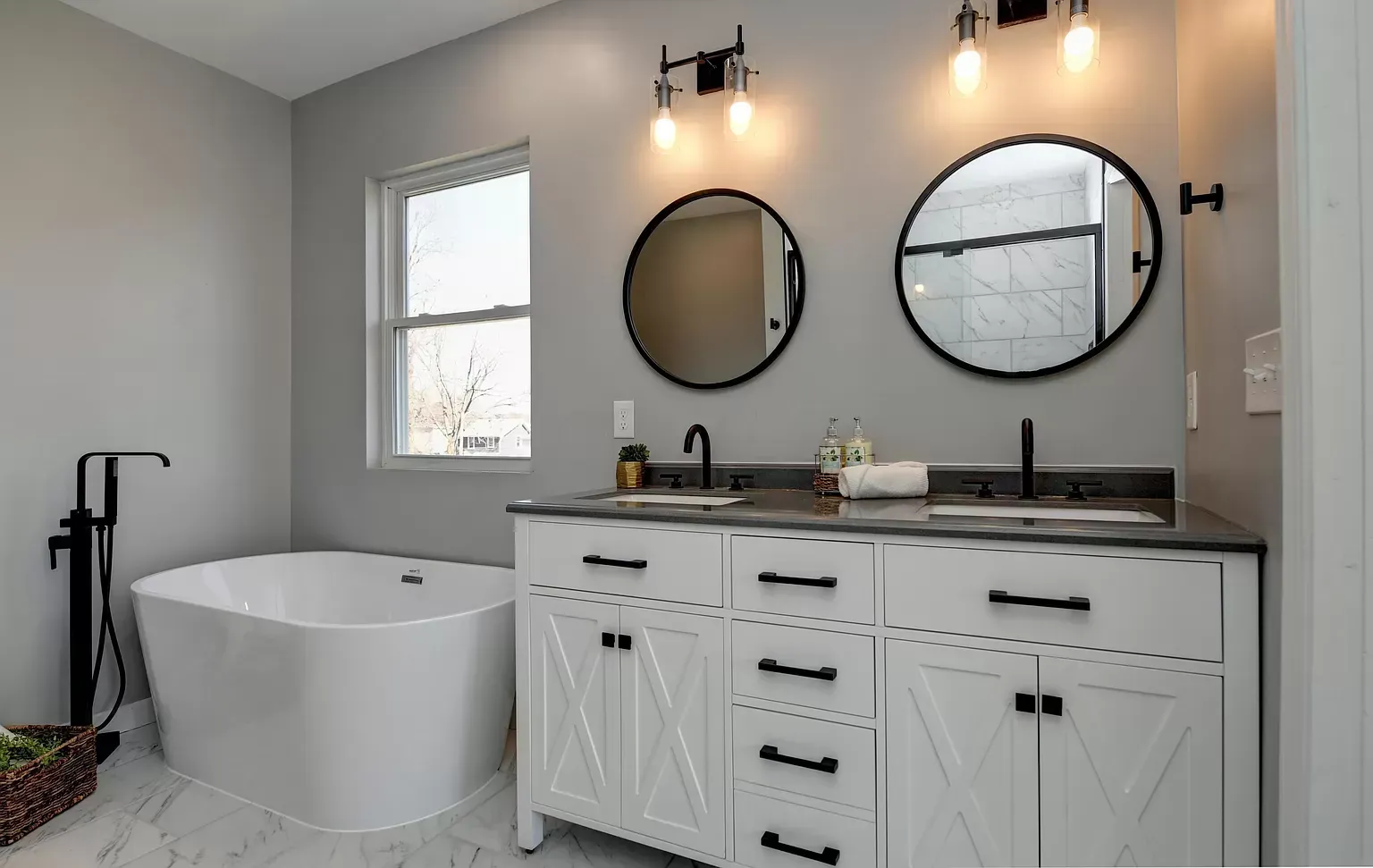 Bathroom with white vanity, black accents, gray walls, soaking tub, and round mirrors.
