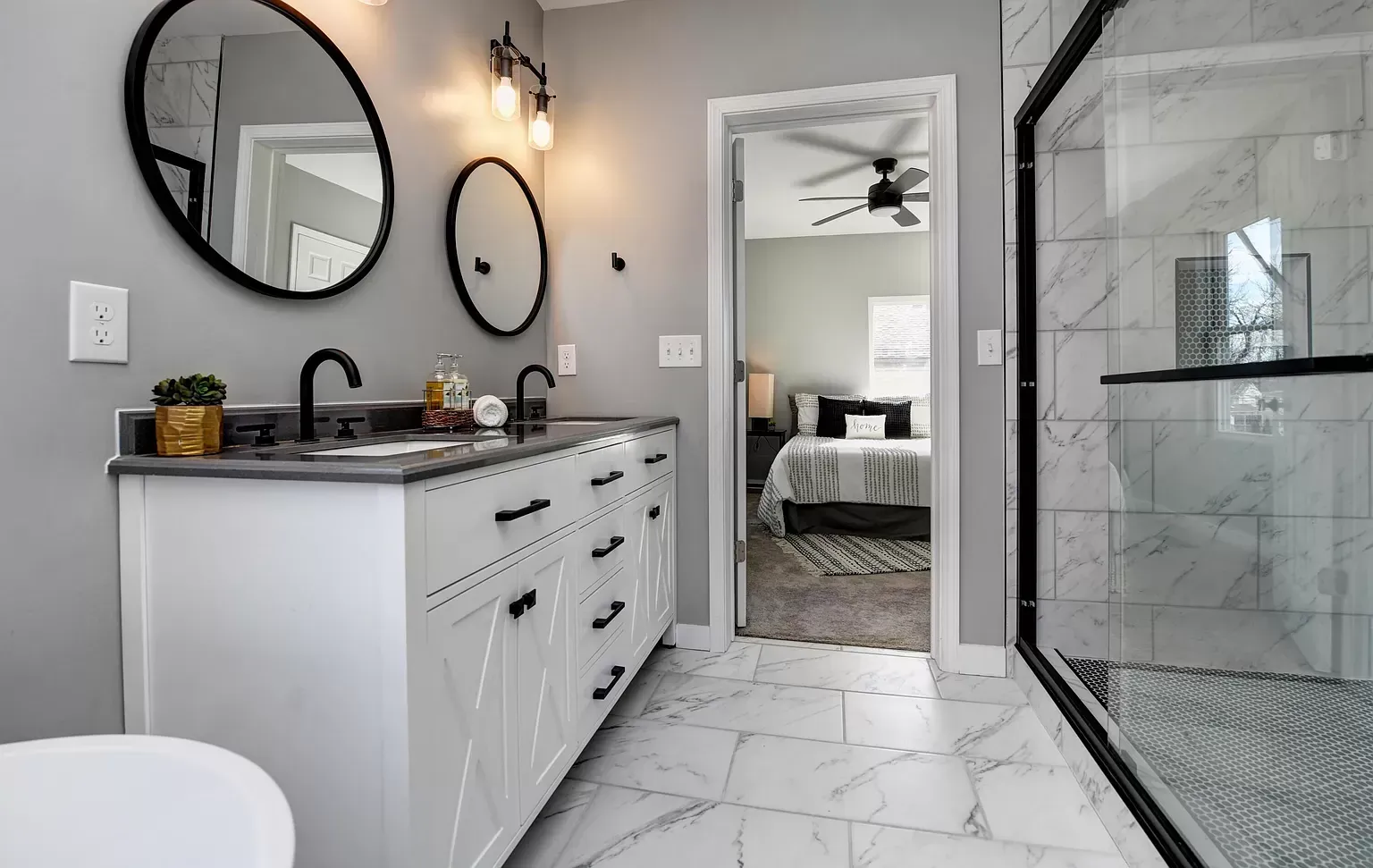 Bathroom with white vanity, black fixtures, and marble tile, with a doorway to a bedroom.