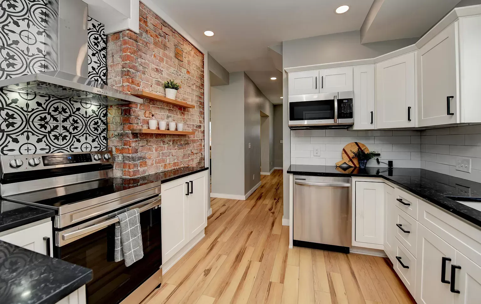 Modern kitchen with white cabinets, black countertops, brick accent wall, and hardwood floors.
