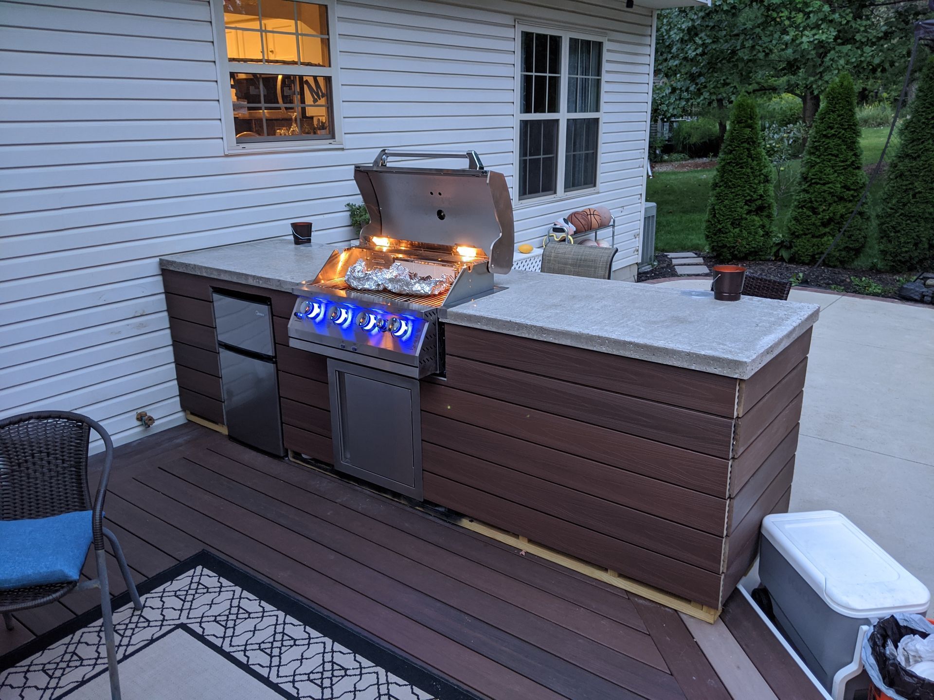 A grill is sitting on a wooden deck in front of a house.