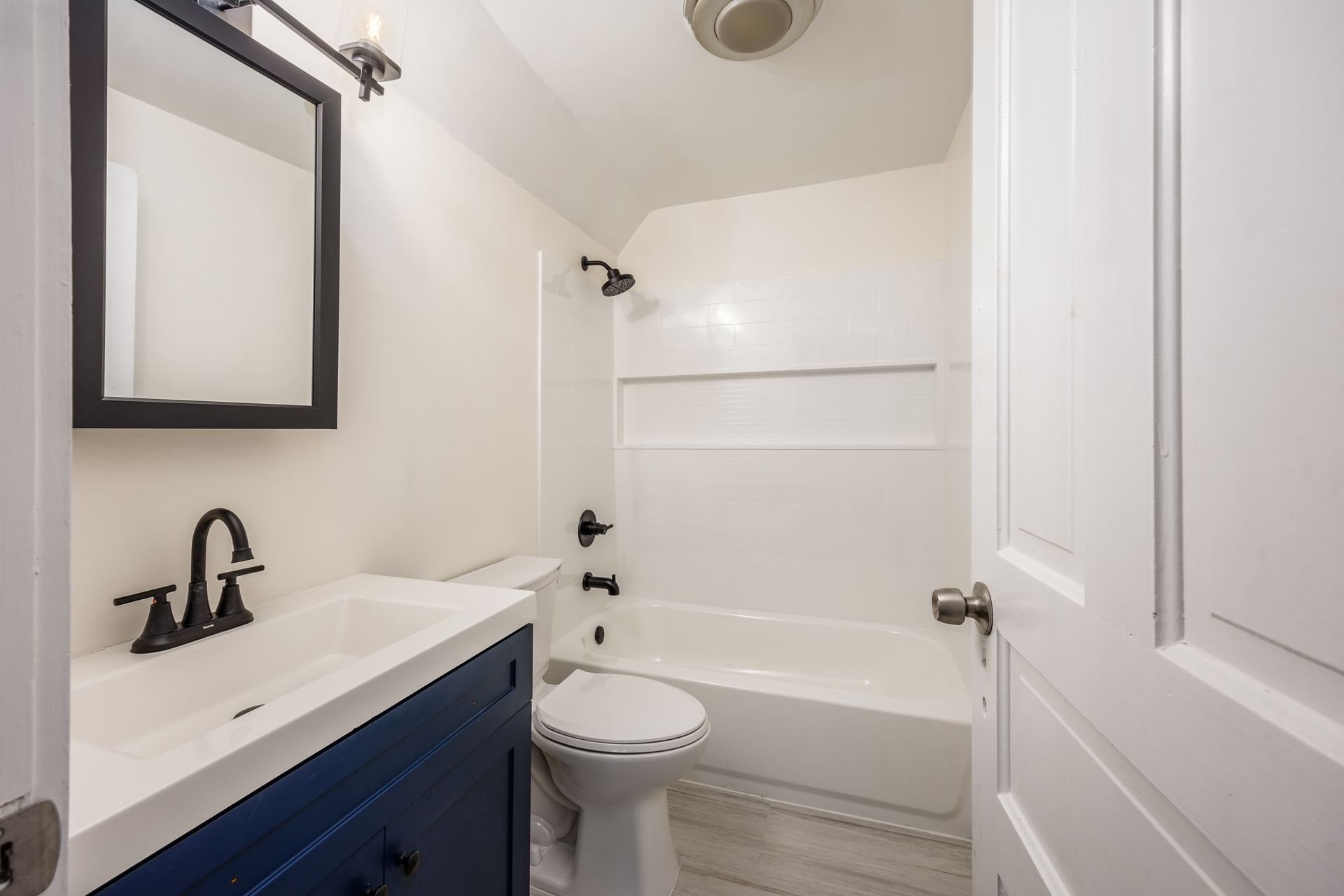 Bathroom with blue vanity, white tub/shower, black faucet, and black-framed mirror.