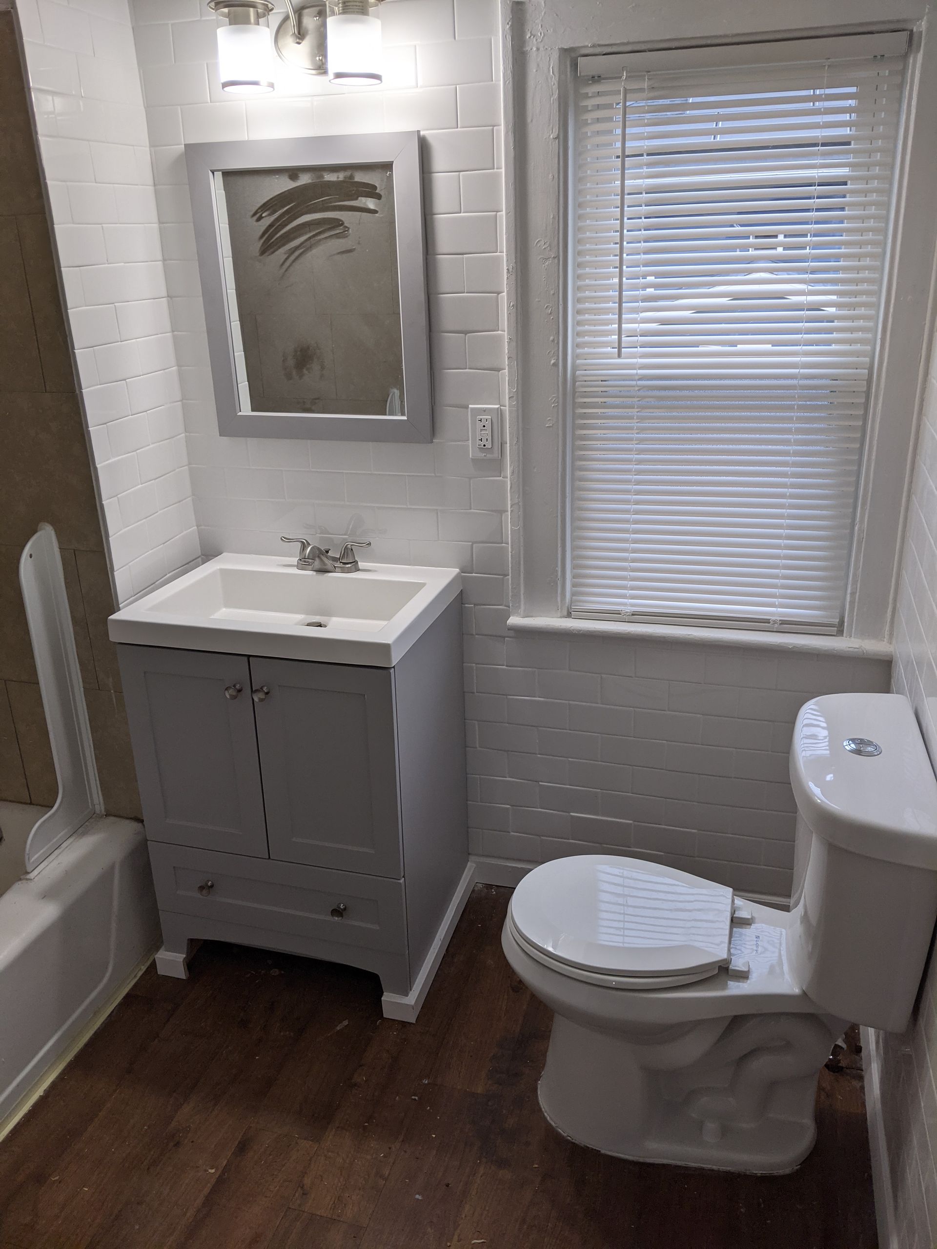 A bathroom with a toilet , sink , mirror and window.