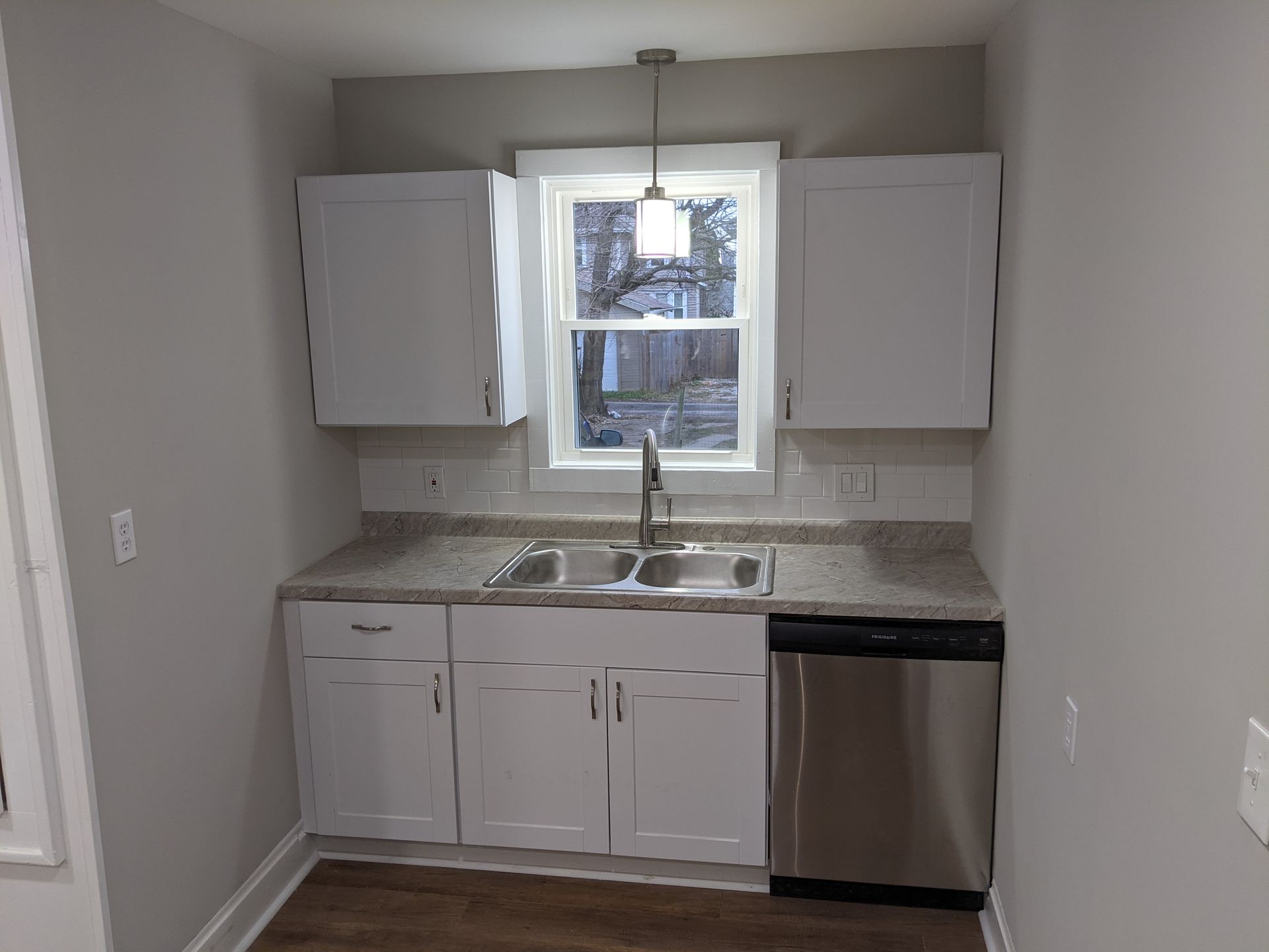 A kitchen with white cabinets , a sink , and a stainless steel dishwasher.