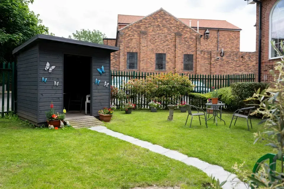 North Hill Residential Care Home, Southey Green, Sheffield | A garden with a shed and a table and chairs in front of a brick building.