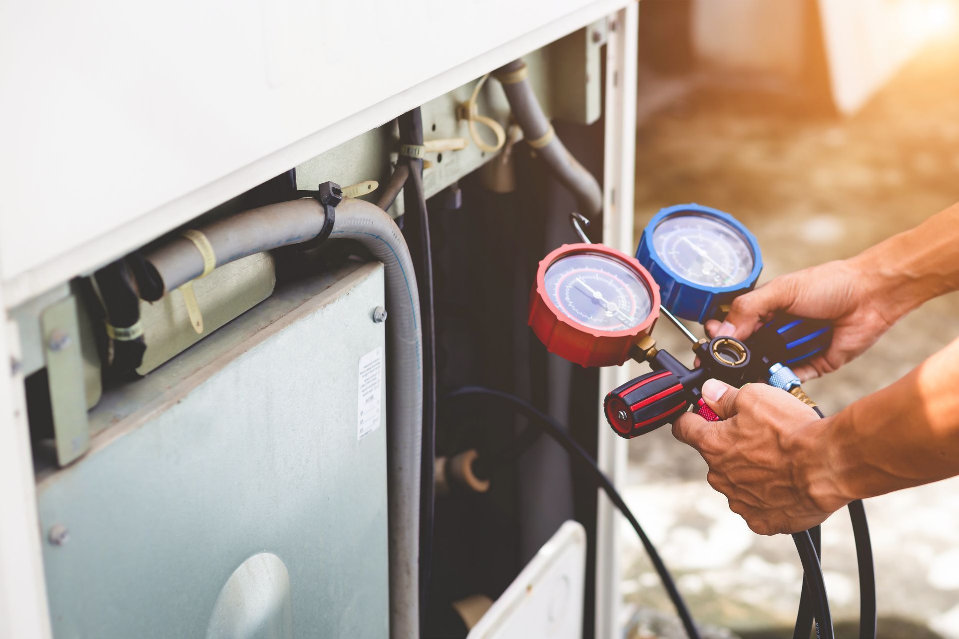 Technician checking HVAC unit pressure with a dual gauge manifold outdoors. Technician checking HVAC unit pressure with a dual gauge manifold outdoors.