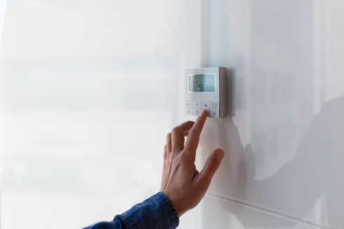 Hand adjusting a wall-mounted thermostat on a white wall. Hand adjusting a wall-mounted thermostat on a white wall.