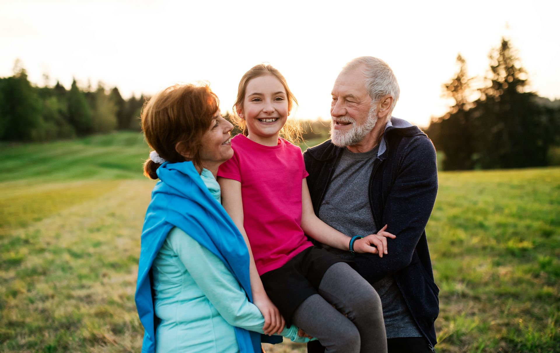 Grandparents holding smiling child in a grassy field.