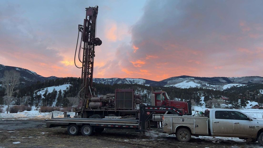 A truck is parked next to a drilling rig in a field.