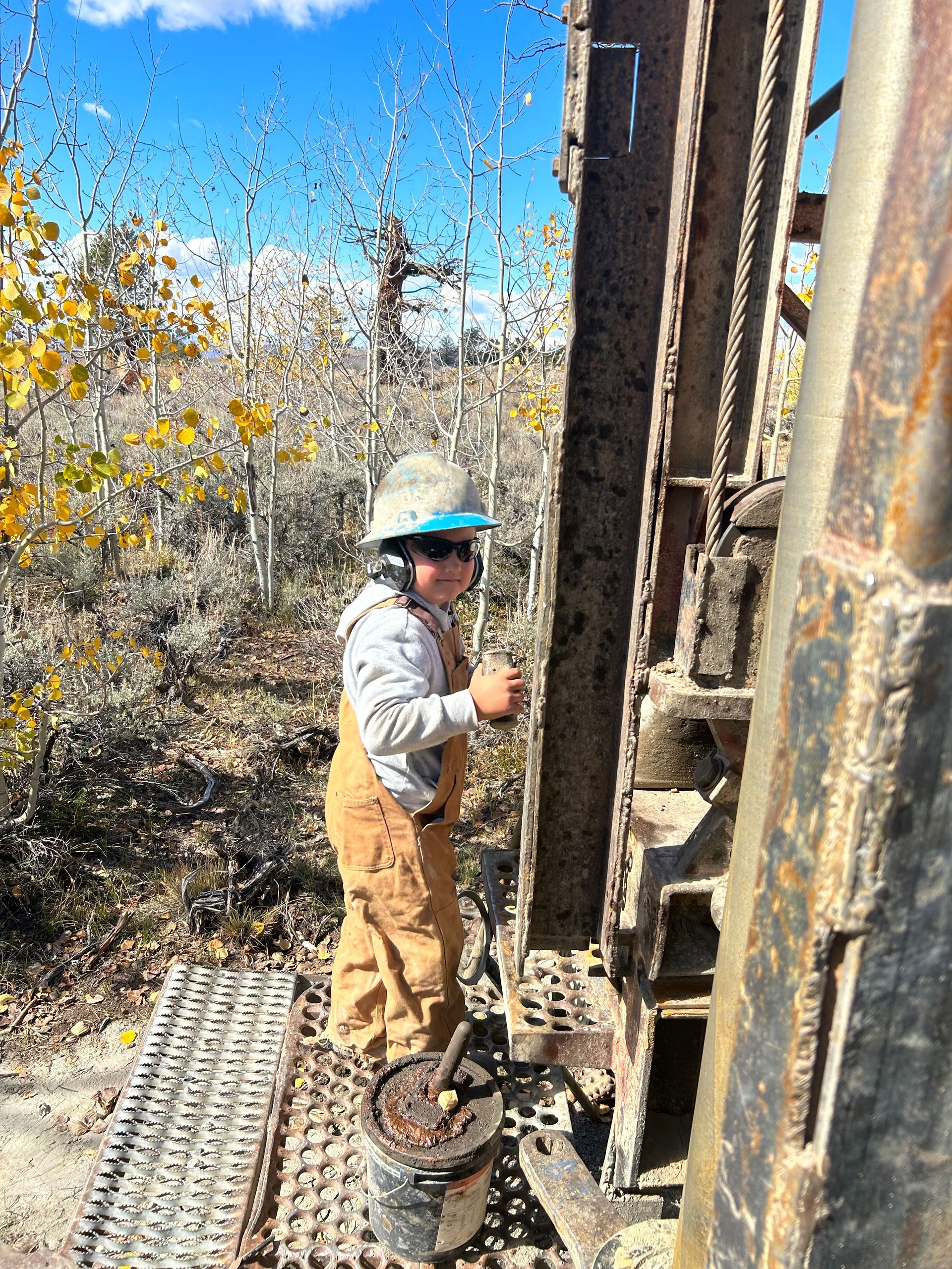 A man wearing a hard hat and overalls is working on a machine.
