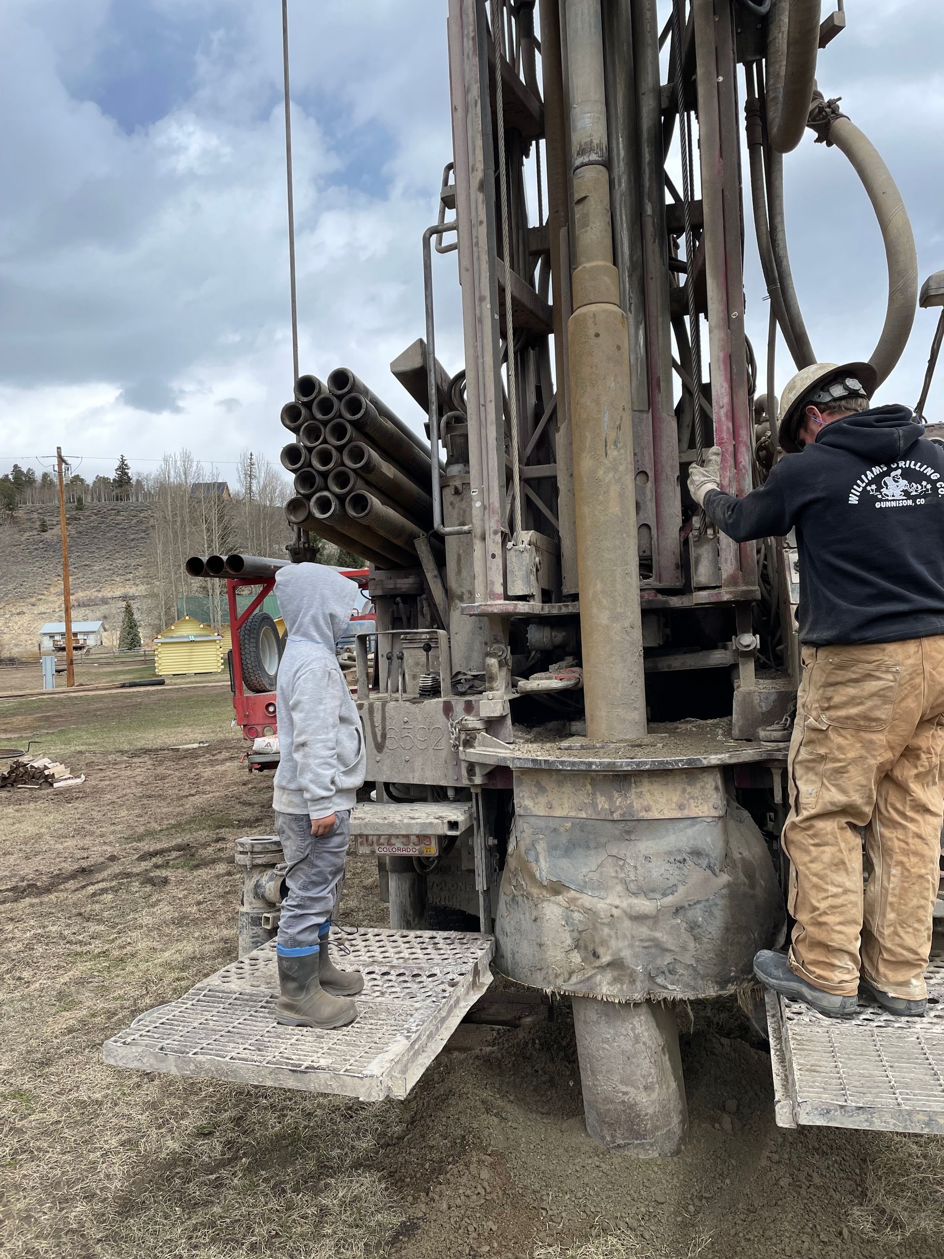 Two men are working on a drilling machine in a field.