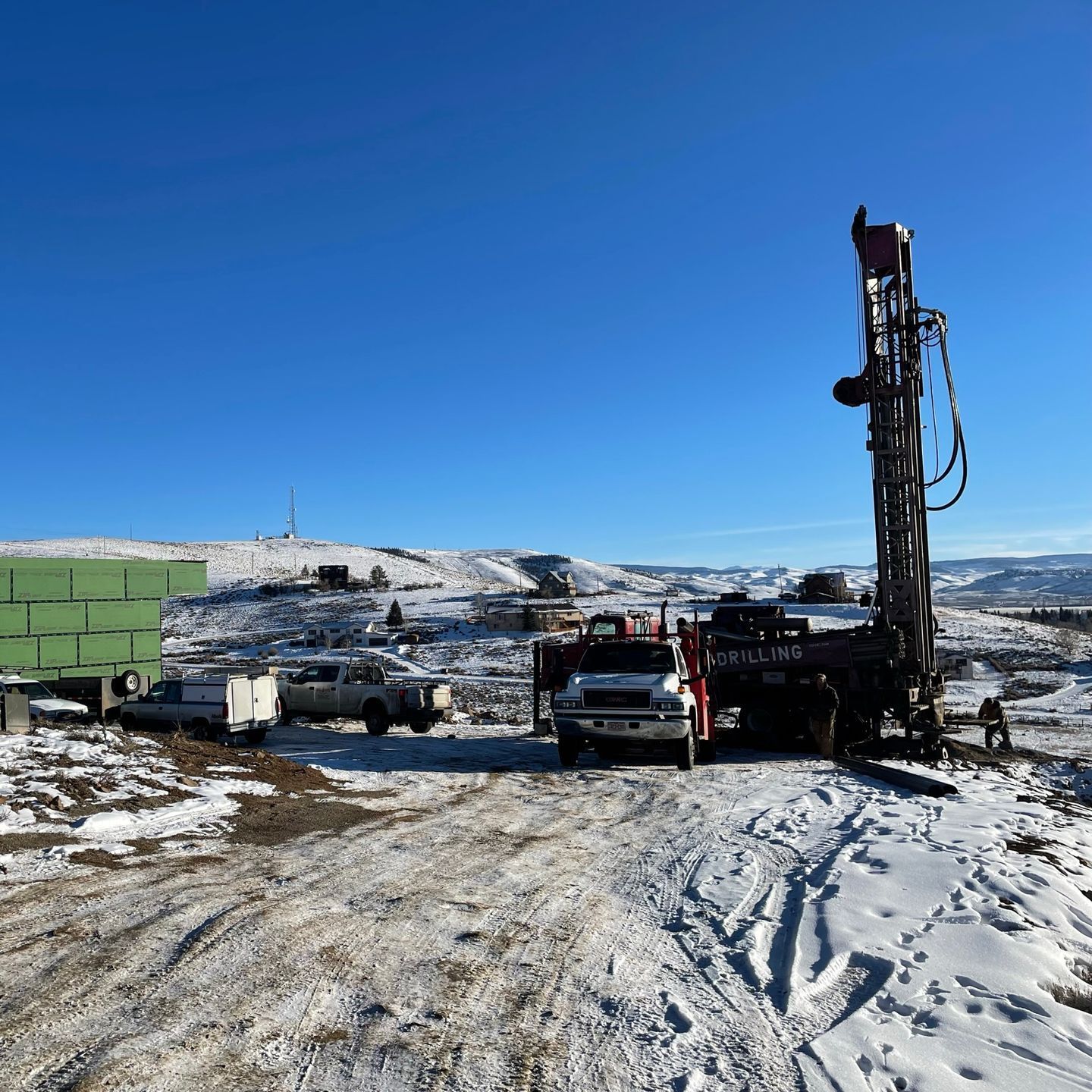 A truck is parked in the snow next to a drill rig