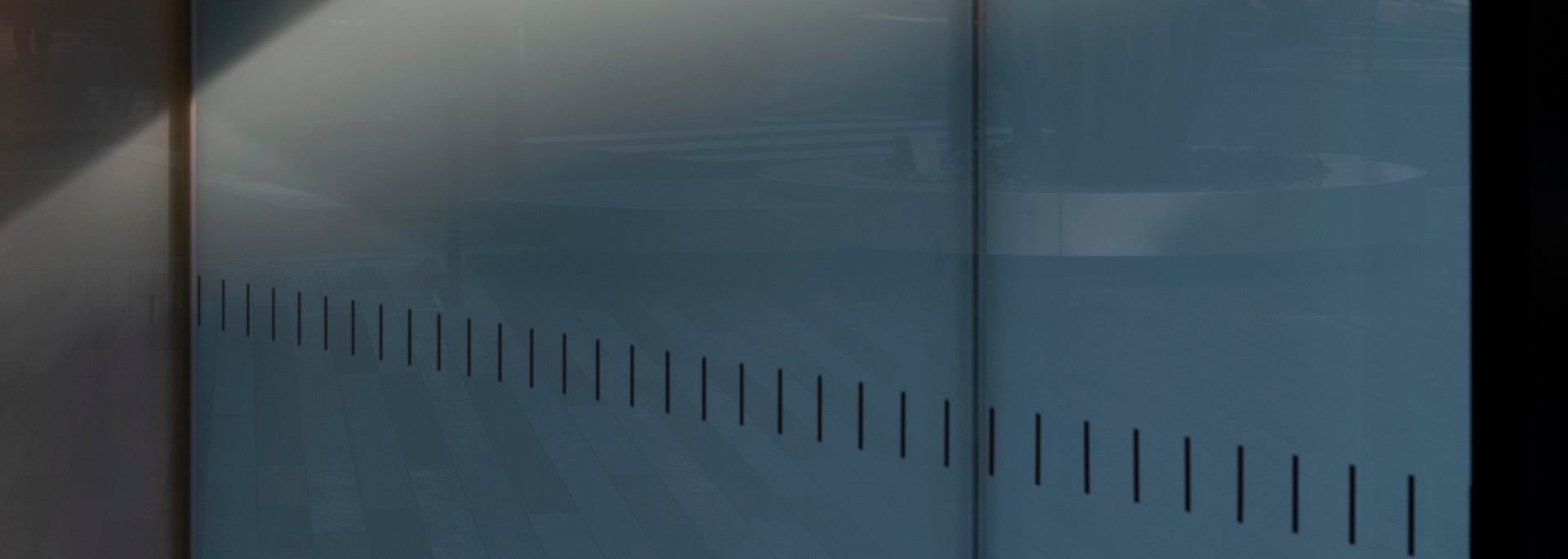 Blue metal wall with evenly spaced vertical slits, lit by a light source at the upper left.