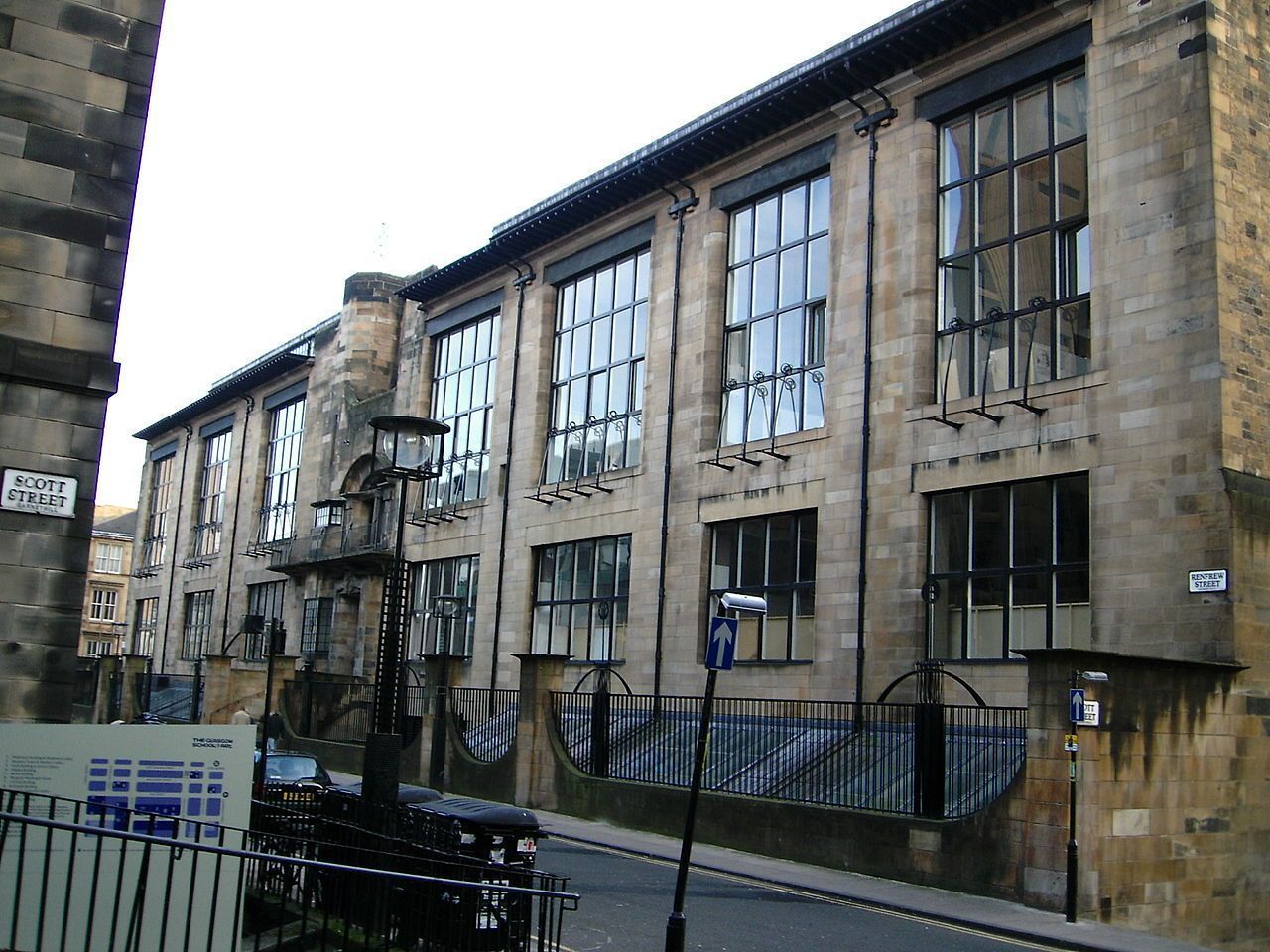 Stone building with tall windows and a black wrought iron fence on a city street.