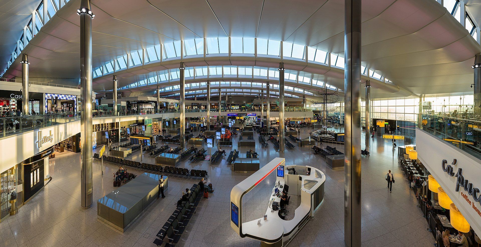 Spacious airport terminal interior with seating areas, shops, and high ceilings.