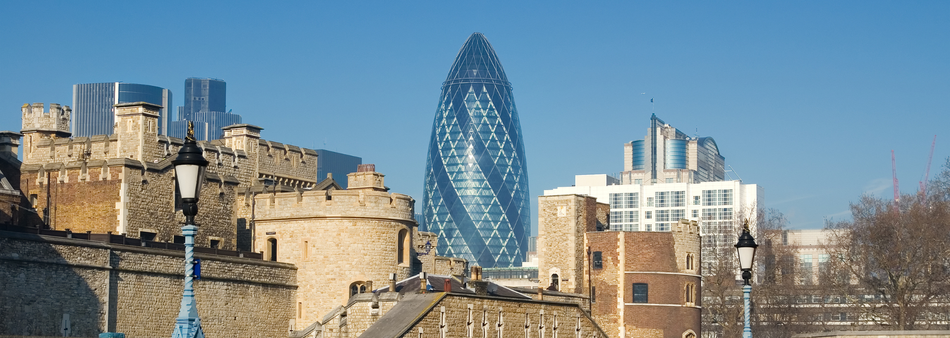 Tower of London with the Gherkin skyscraper in the background against a blue sky.