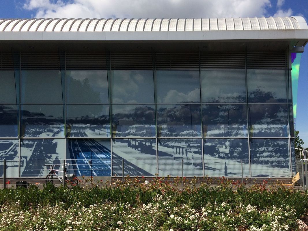 Exterior of a modern building with reflective glass panels showing a snowy mountain scene. A train track is visible below.