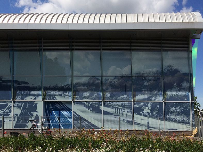 Building facade with a reflective glass mural of a train station, blue and gray tones.