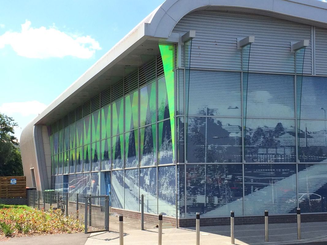 Modern building with large glass panels displaying a mountain scene, green accents, and a curved roof.