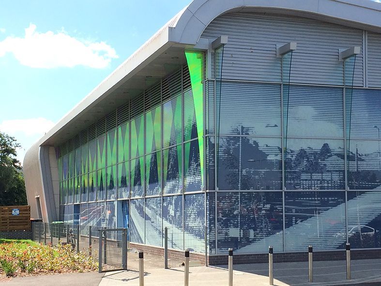 Modern building with glass facade, featuring green accents and a panoramic scene, under a bright sky.