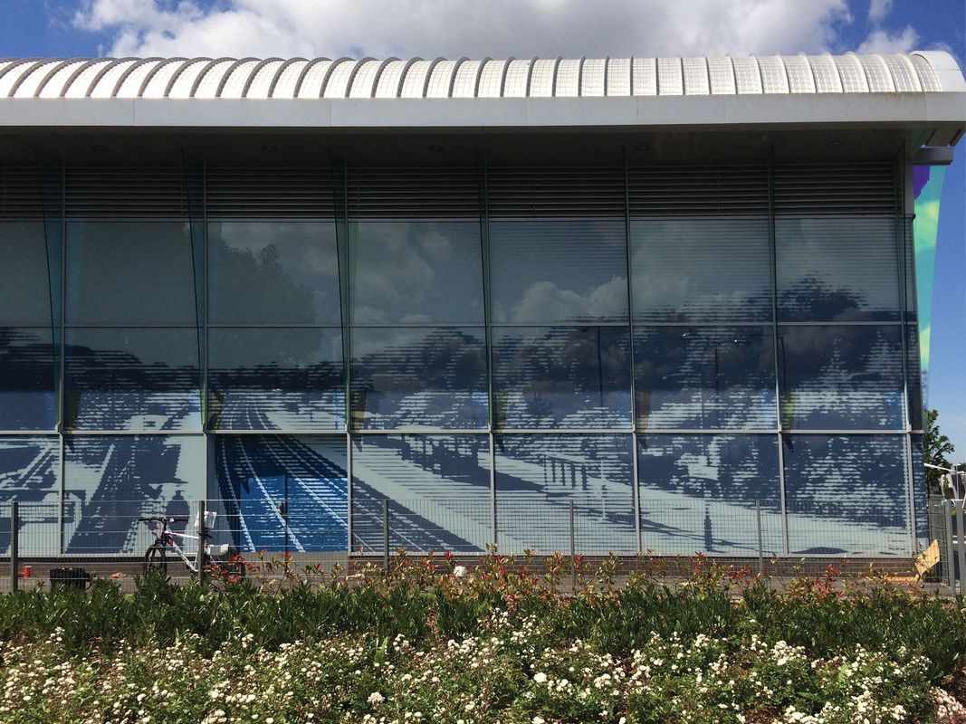 Exterior of a building with large glass windows reflecting a train station and sky.