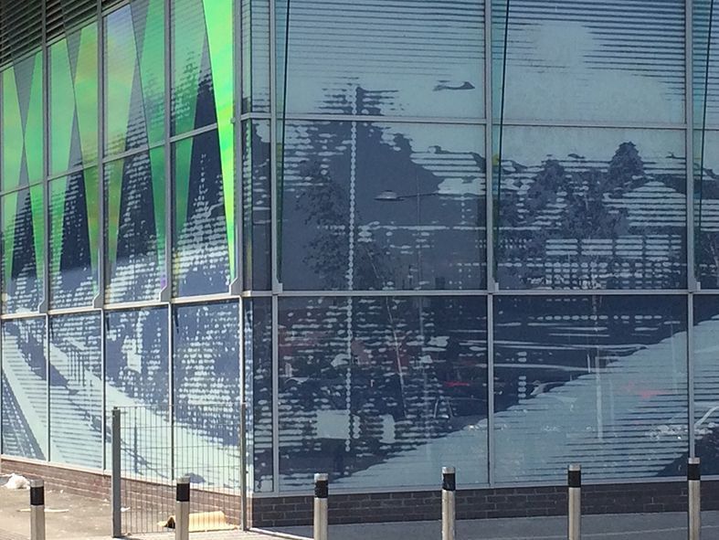 Glass building facade with green and blue color patterns reflecting the exterior environment.