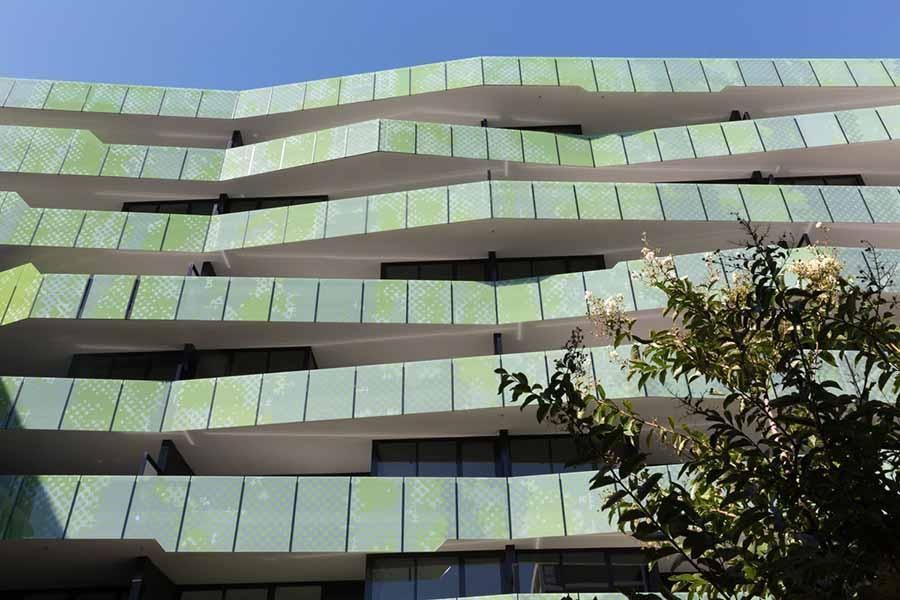 Modern apartment building with wavy green and white balconies under a blue sky.