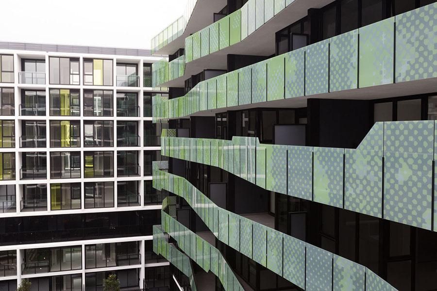 Modern building exterior with curved balconies, green patterned panels, and rectangular windows.