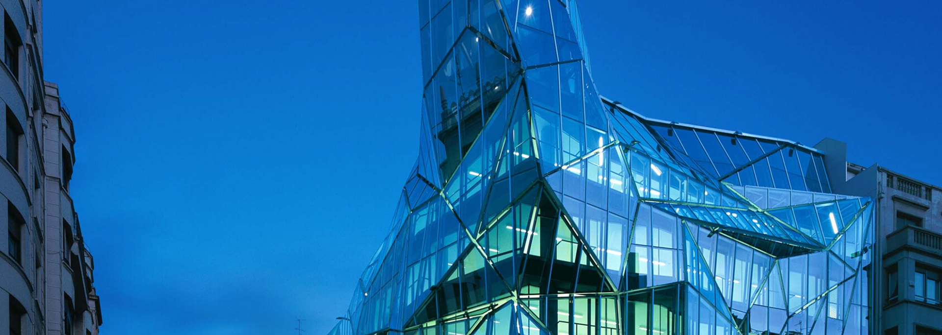 A modern glass skyscraper against a blue twilight sky.