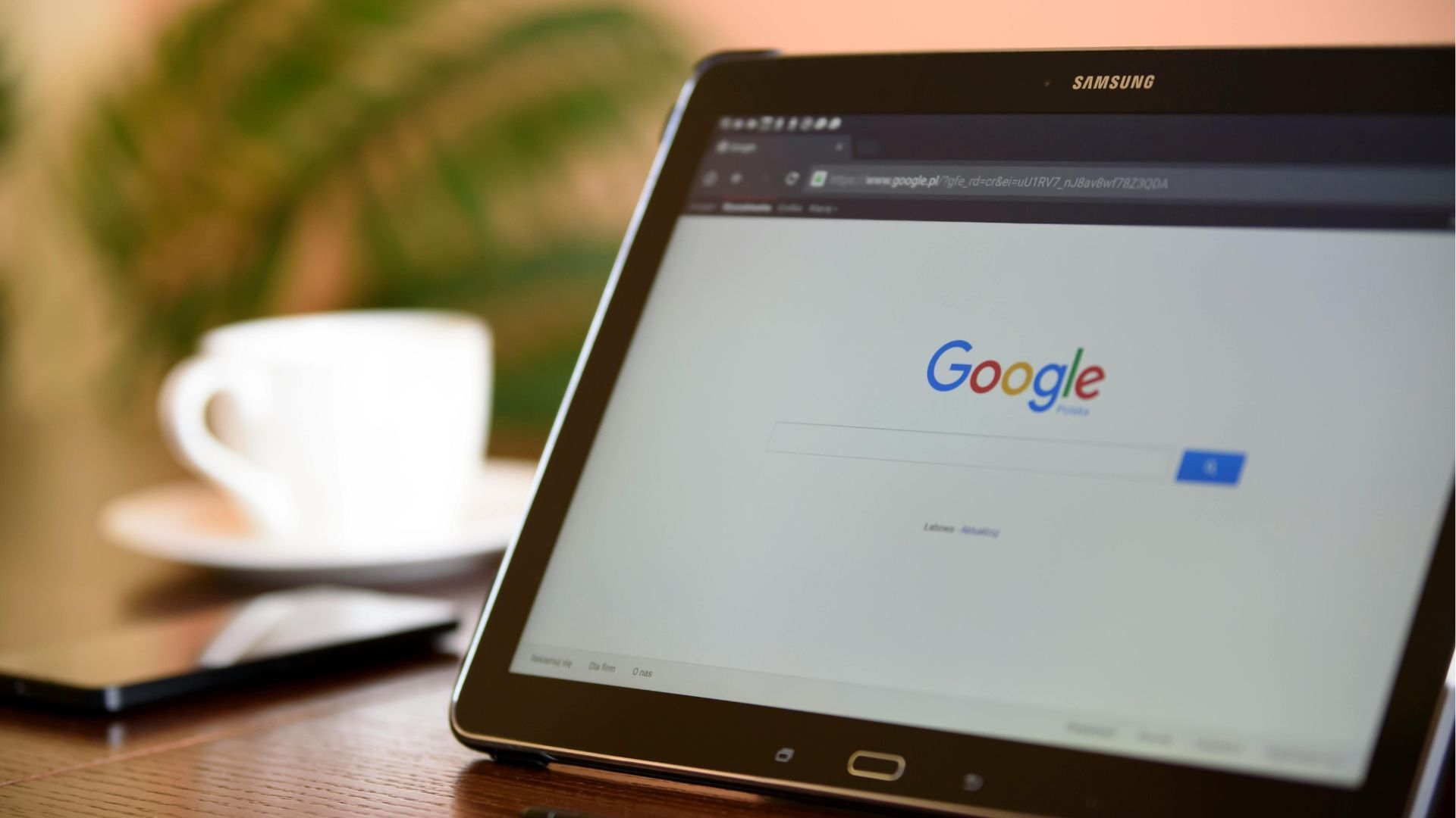 Tablet displaying the Google search page on a wooden table, next to a white coffee cup.