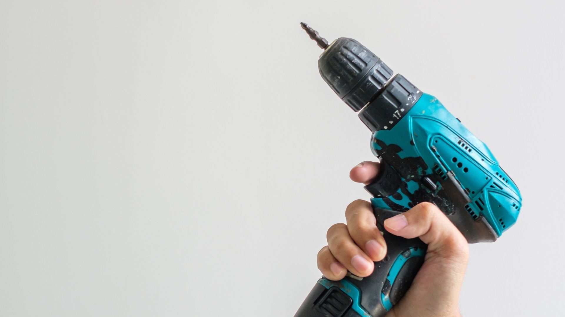 Hand holding a teal and black cordless drill, against a white background.