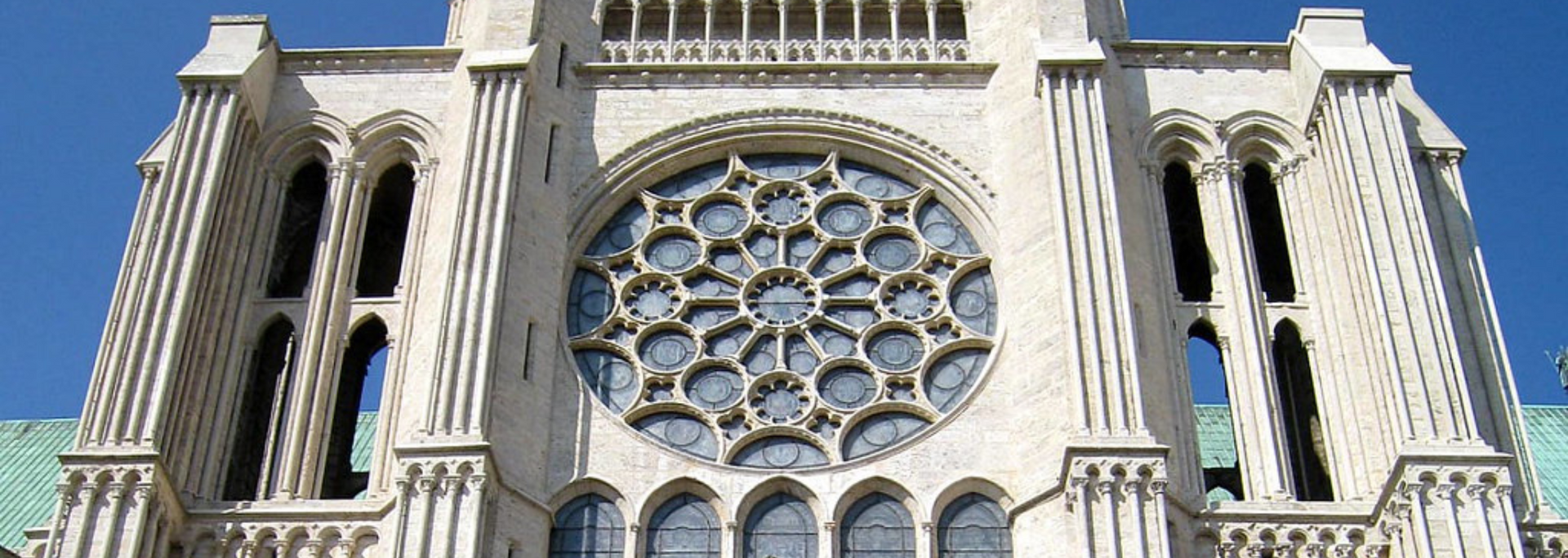 Exterior view of a cathedral with a large rose window and architectural details against a blue sky.