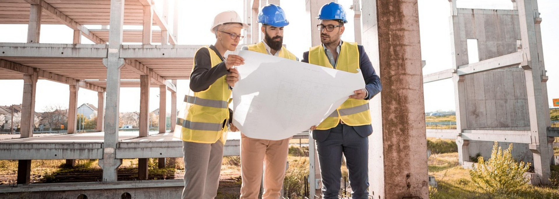 Three construction workers in hard hats reviewing a blueprint on a construction site.