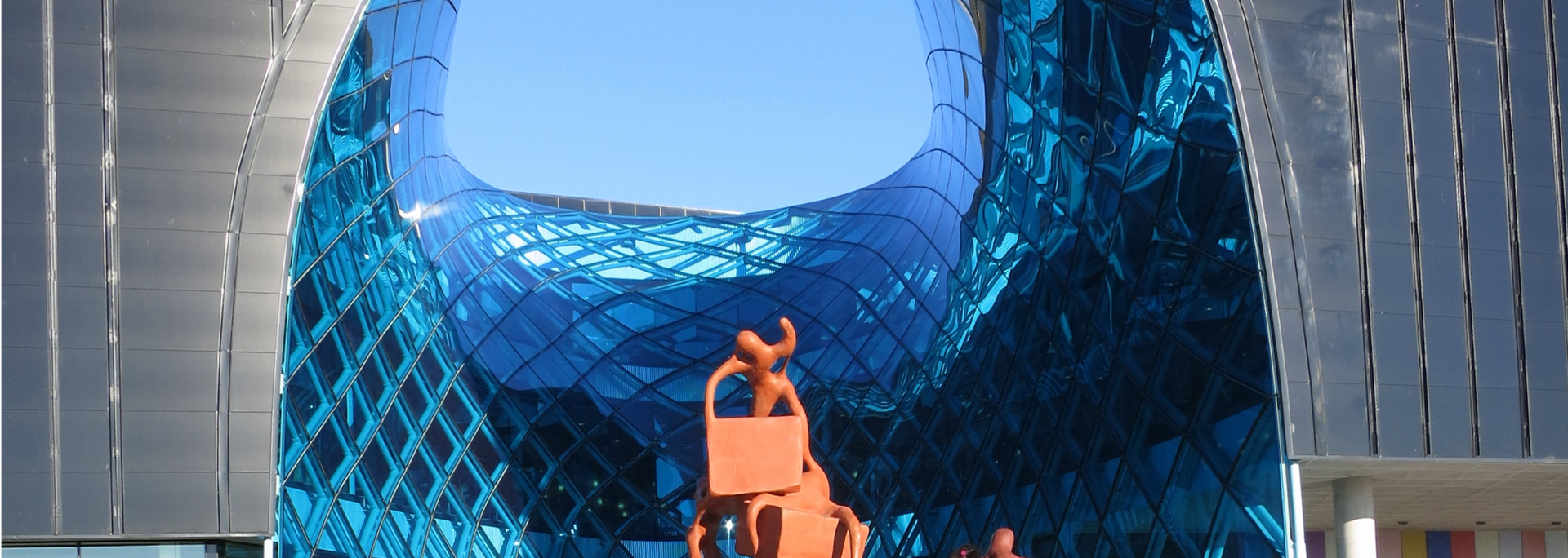 A sculpture of two figures against the background of a blue building under a blue sky.