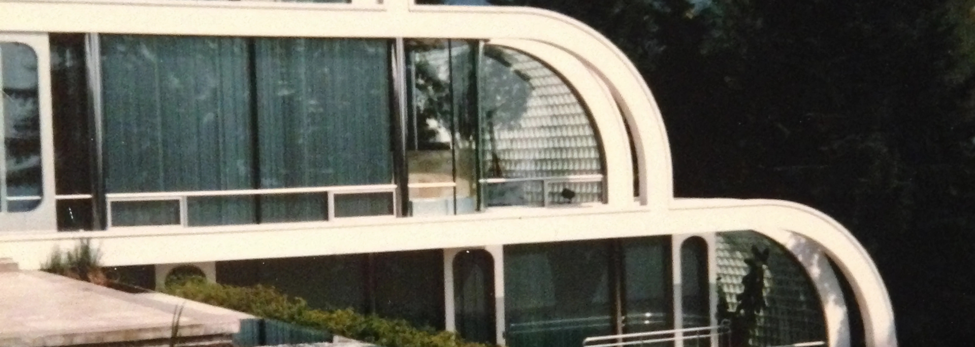 Modern white building with arched glass windows and a lush green backdrop.
