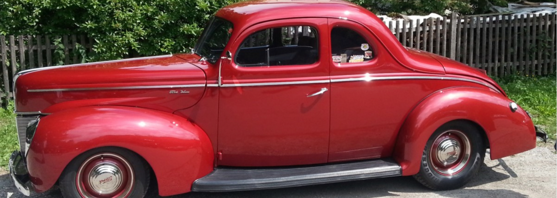 Red classic car parked in front of a wooden fence.