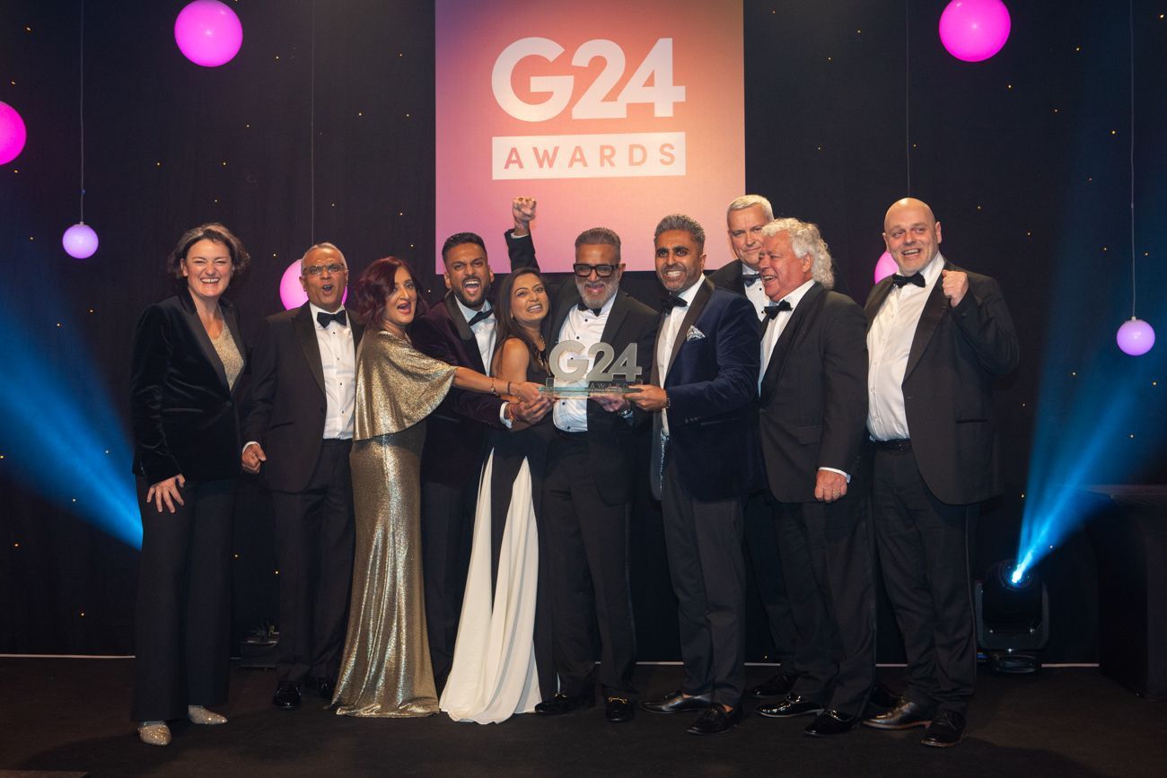 Group of people holding an award on a stage, under G24 Awards sign, celebrating.