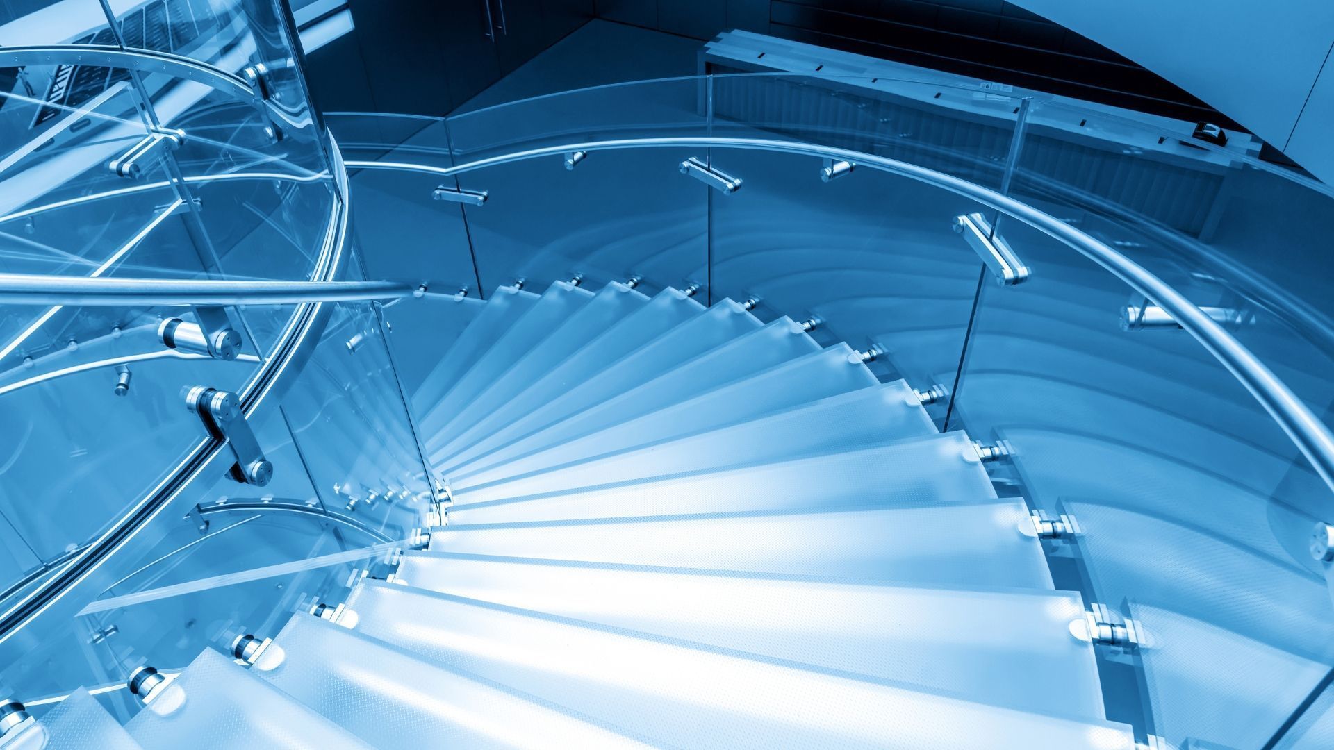 Blue-toned spiral staircase with glass steps and metal handrails, viewed from above.