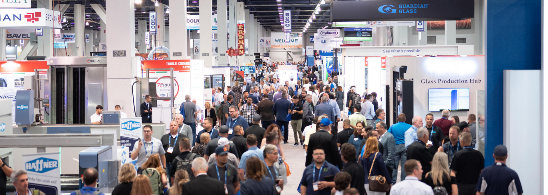 Crowd of people walking through a convention center, several booths visible.