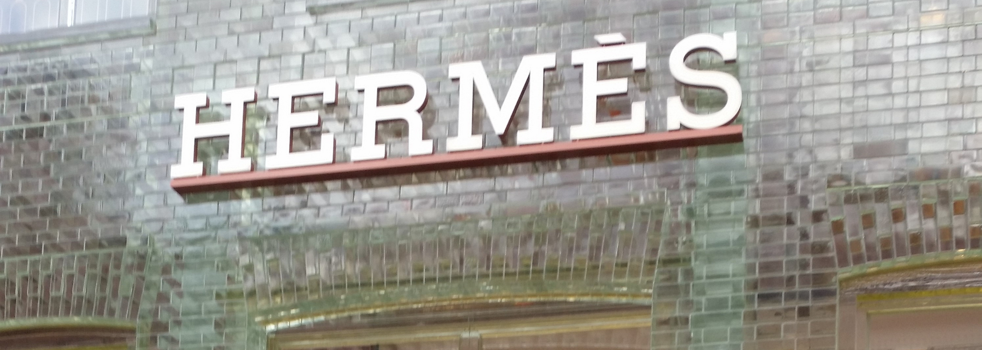 Hermès store sign on a brick wall. White letters with a brown trim.