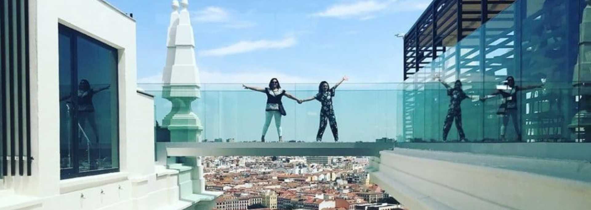 People holding hands with arms outstretched on a glass walkway overlooking a city.