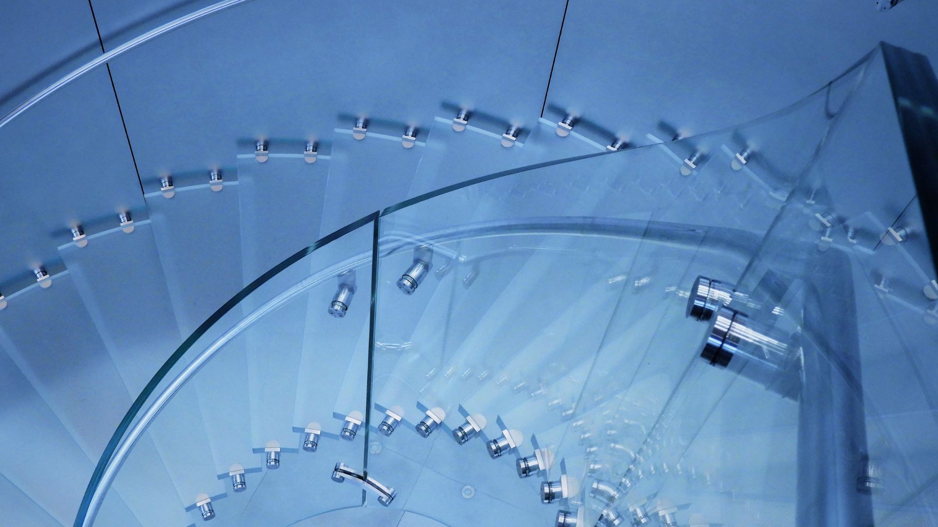 Curved glass staircase with metal supports; blue-toned overhead view.